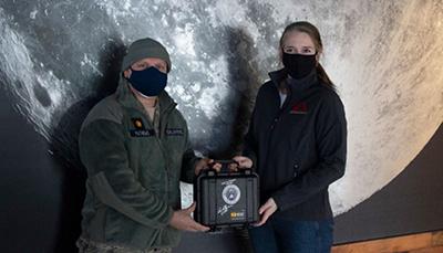 Major James Mathews of Civil Air Patrol hands over the encased microchip to Alivia Chapla, Astrobotic's Senior Marketing and Communications Specialist.